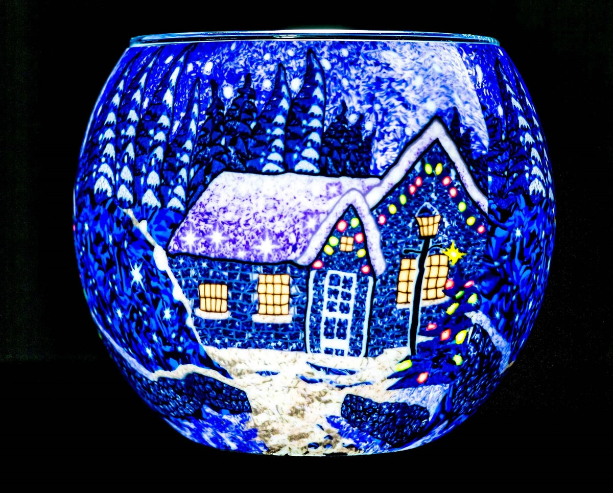 Winter Wonderland Claymaster light globe glowing cobalt blue with a snowy cottage, lit windows, decorated tree and frosted evergreens