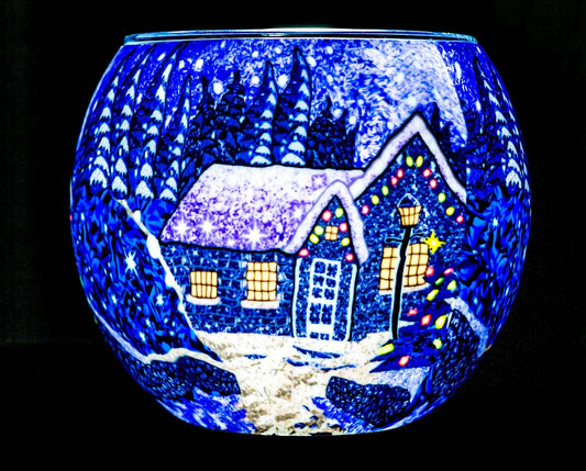 Winter Wonderland Claymaster light globe glowing cobalt blue with a snowy cottage, lit windows, decorated tree and frosted evergreens
