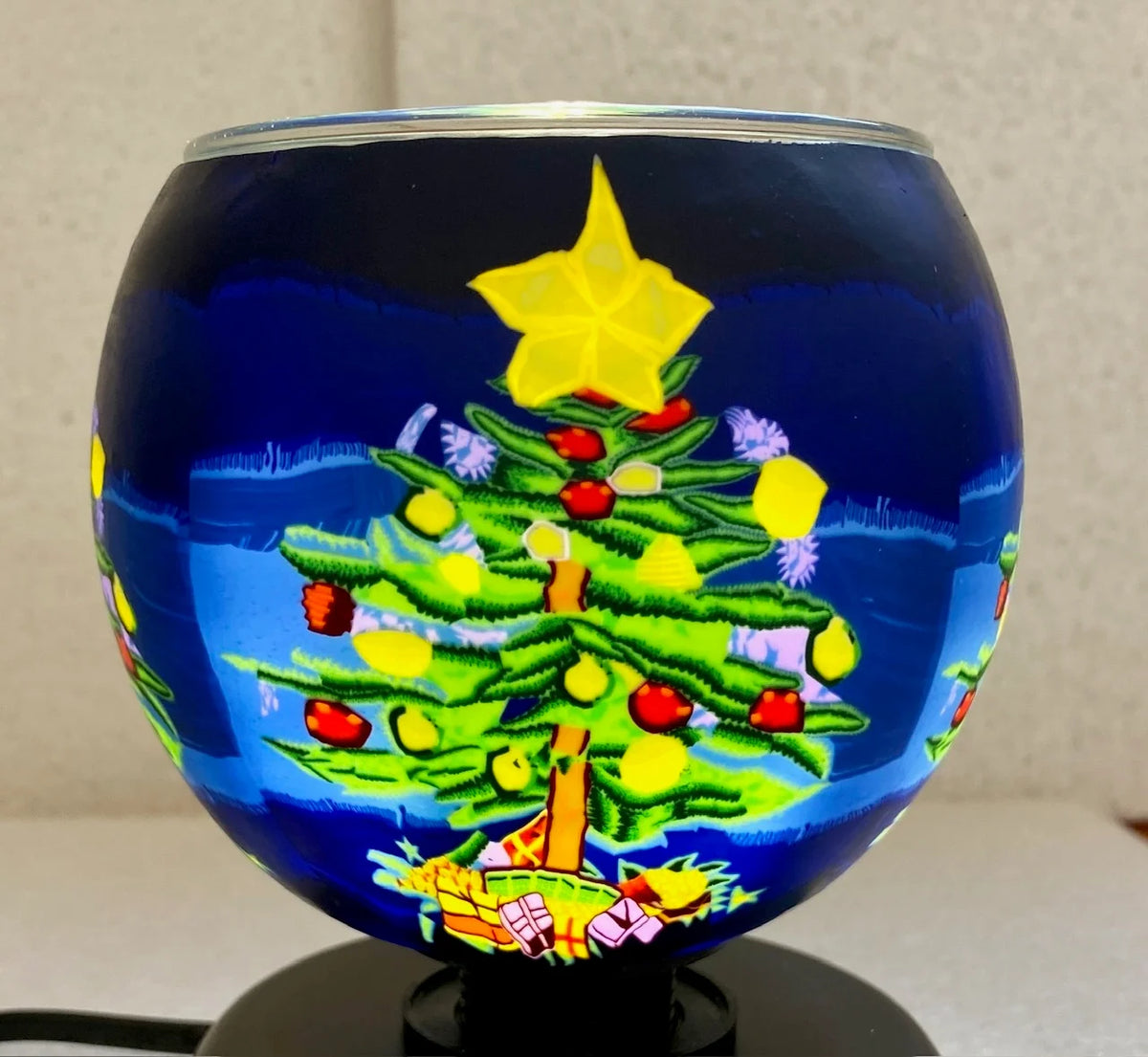 Claymaster Christmas Tree light globe glowing on a black base, showing a decorated tree with star topper and presents in snow